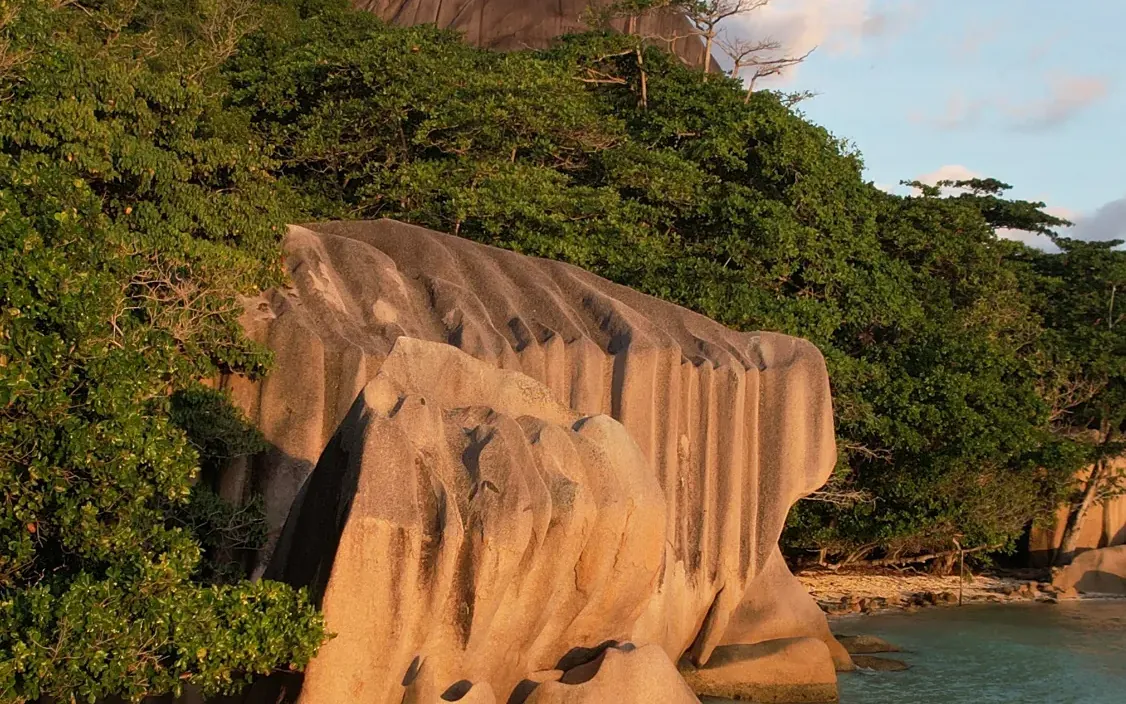Couple walking the beach beside the granite boulders in golden light