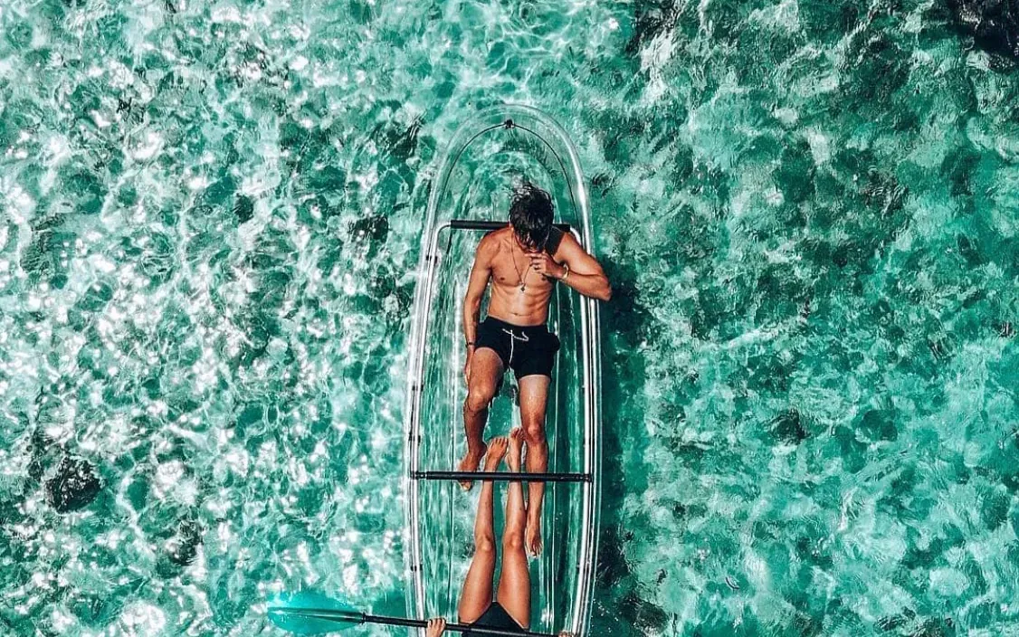Two guests lying in one transparent kayak seen from above