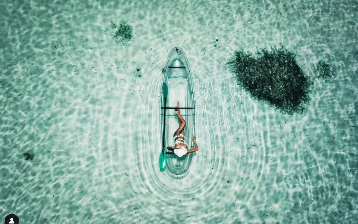 Aerial view of a clear kayak on pale green water above a coral patch