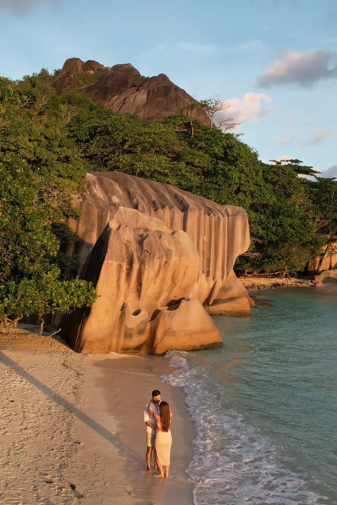 Couple walking the beach beside the granite boulders in golden evening light