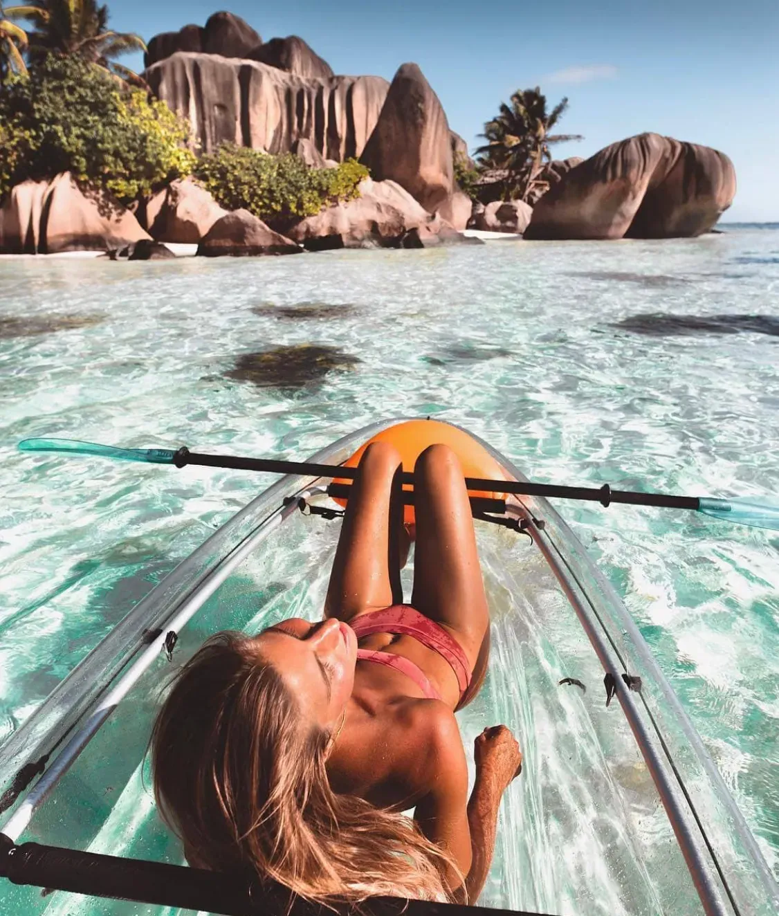 Guest lying back in a clear kayak with boulders and palms behind