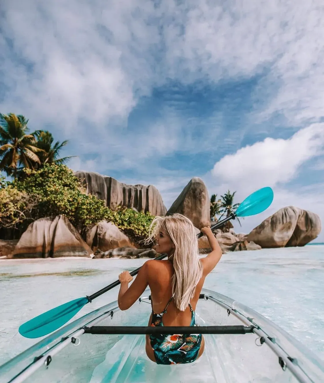 Guest paddling a transparent kayak toward the granite boulders and palms