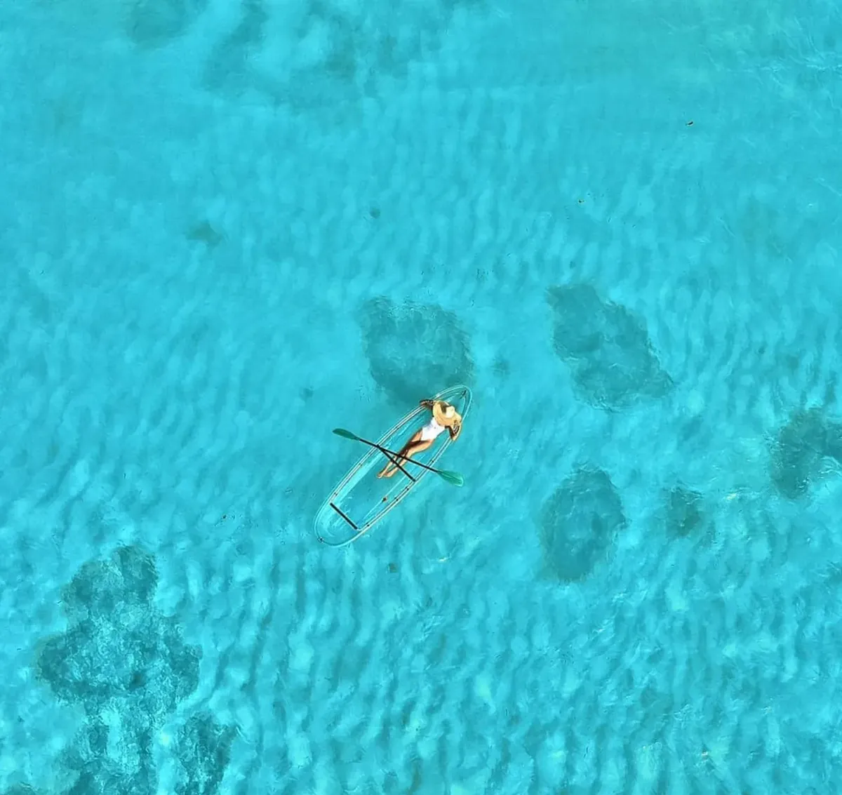 A tiny clear kayak on vivid turquoise water beside dark coral patches