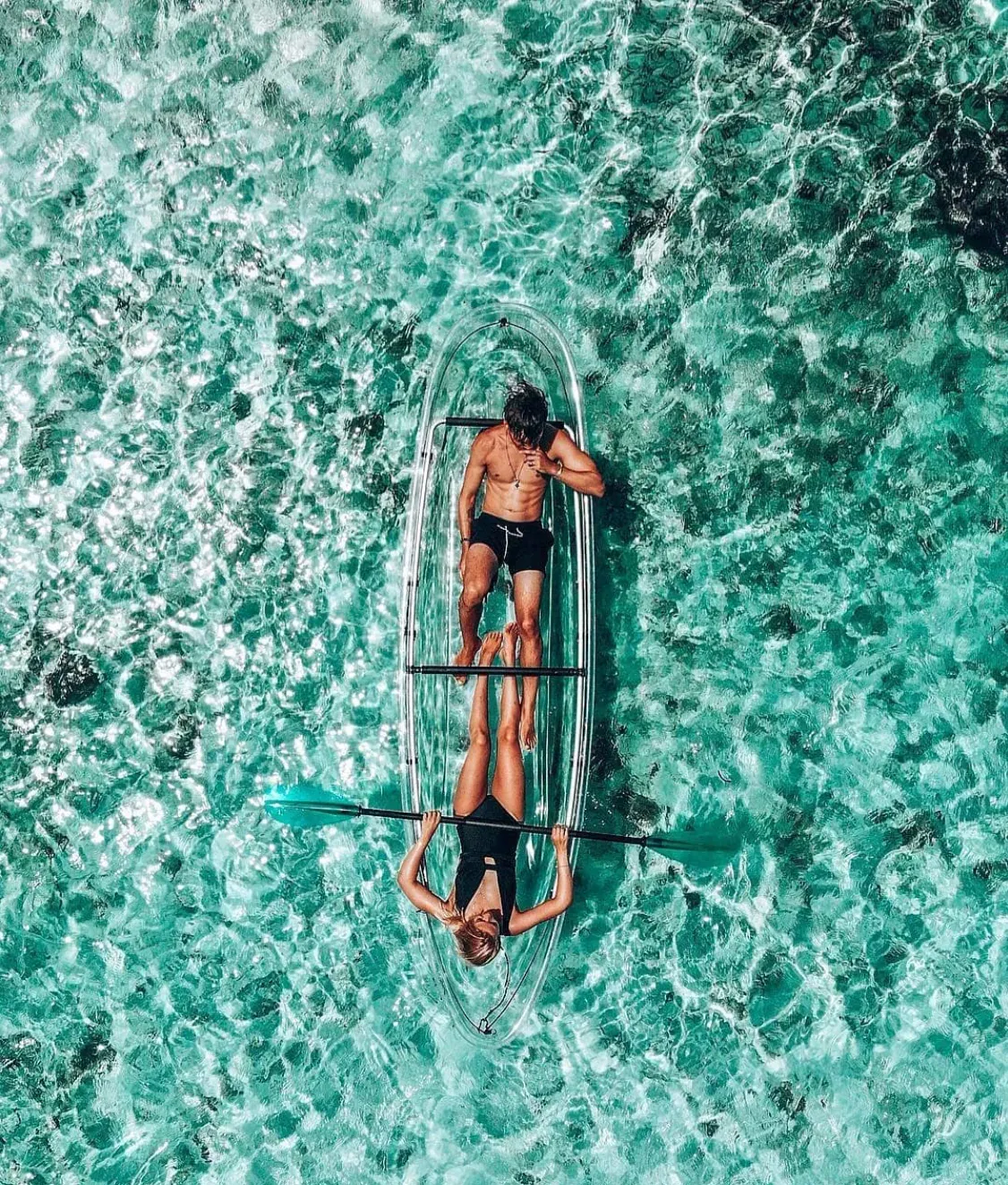 Two guests lying in one transparent kayak seen from directly above