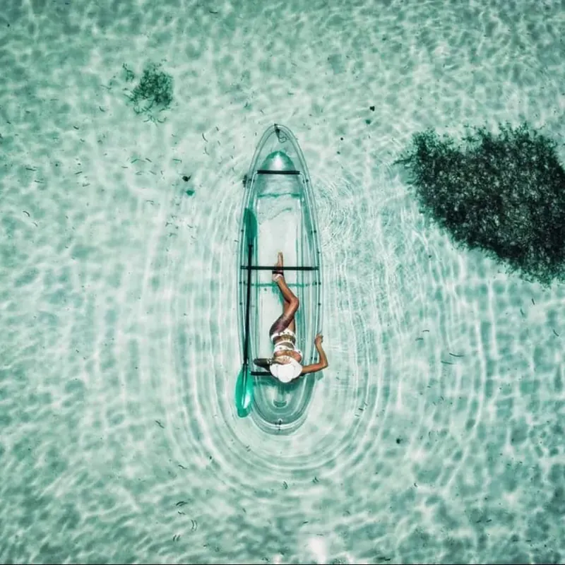 Aerial view of a clear kayak on pale green water above a coral patch