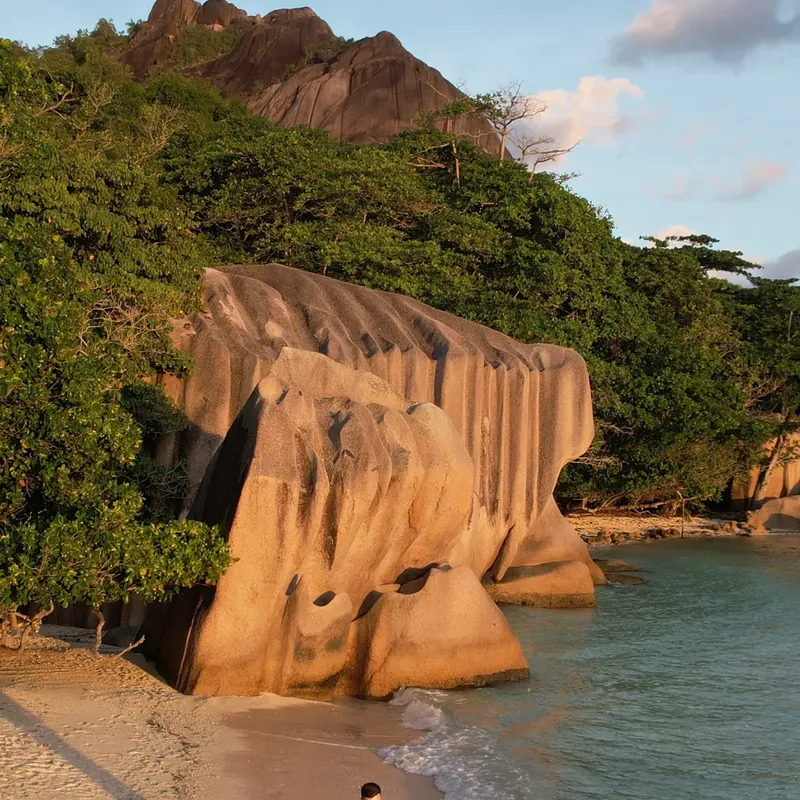 Couple walking the beach beside the granite boulders in golden evening light