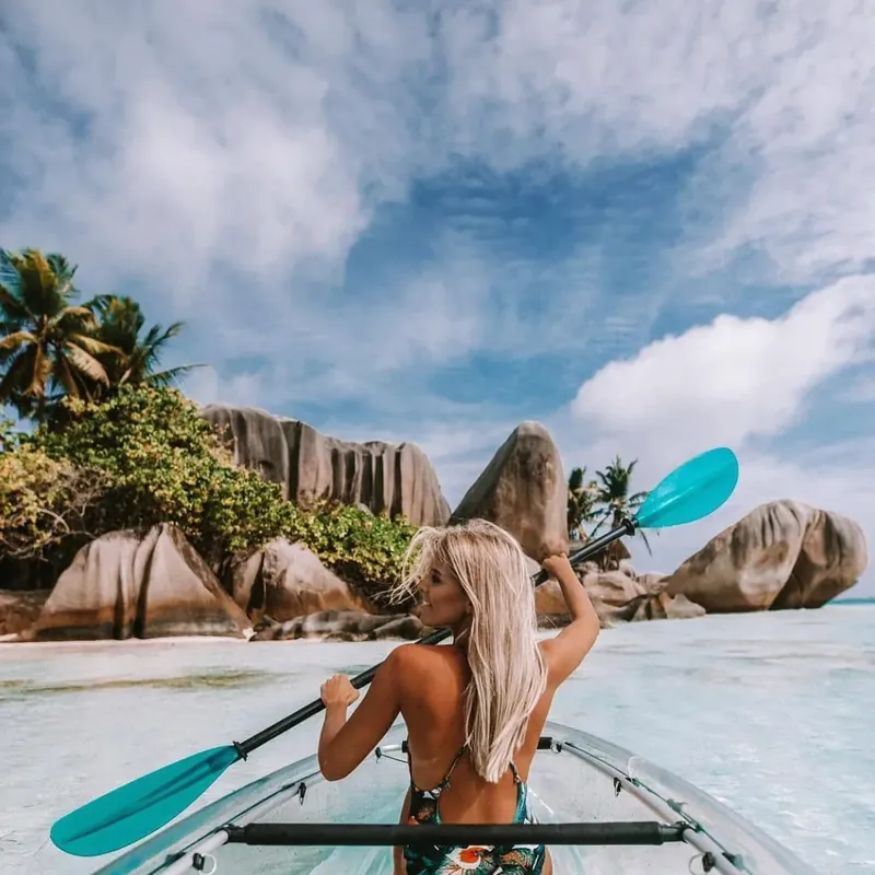Guest paddling a transparent kayak toward the granite boulders and palms