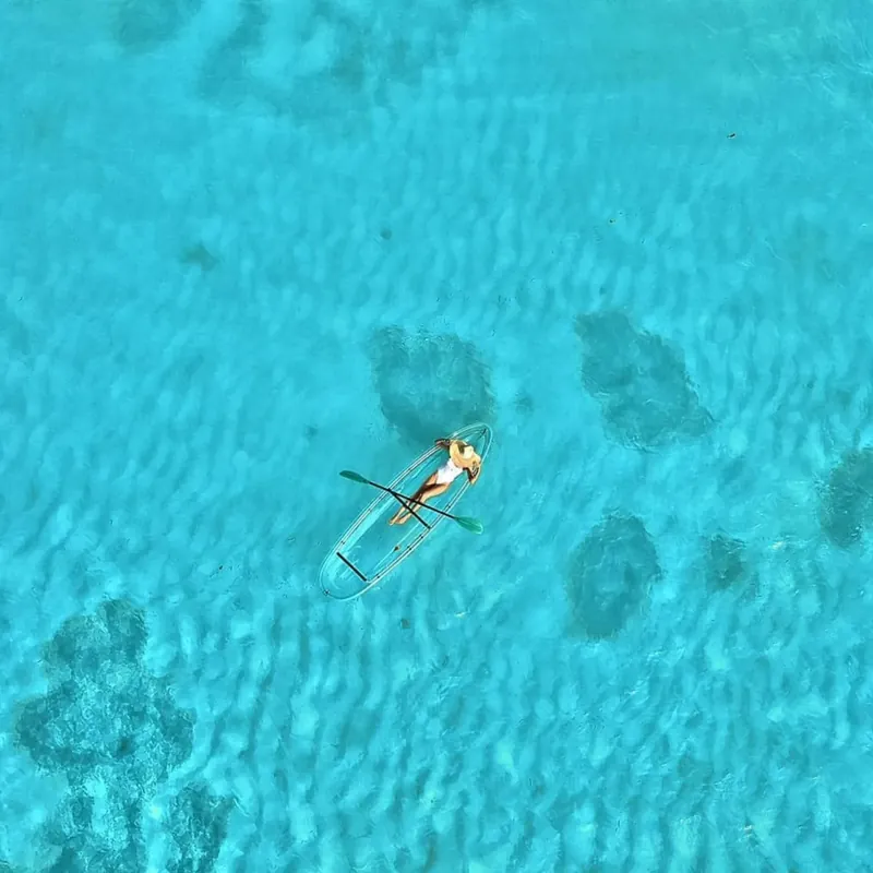 A tiny clear kayak on vivid turquoise water beside dark coral patches
