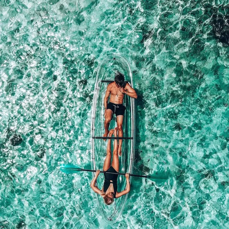 Two guests lying in one transparent kayak seen from directly above